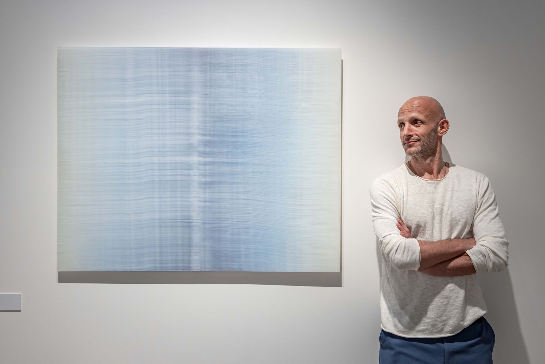 An artist standing beside his work in a gallery