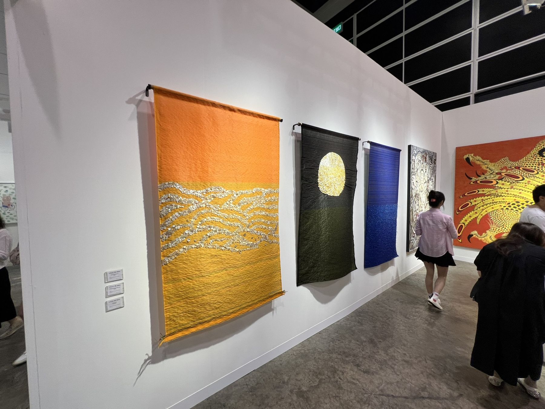 Visitors walking past large woven textile works in an art fair booth