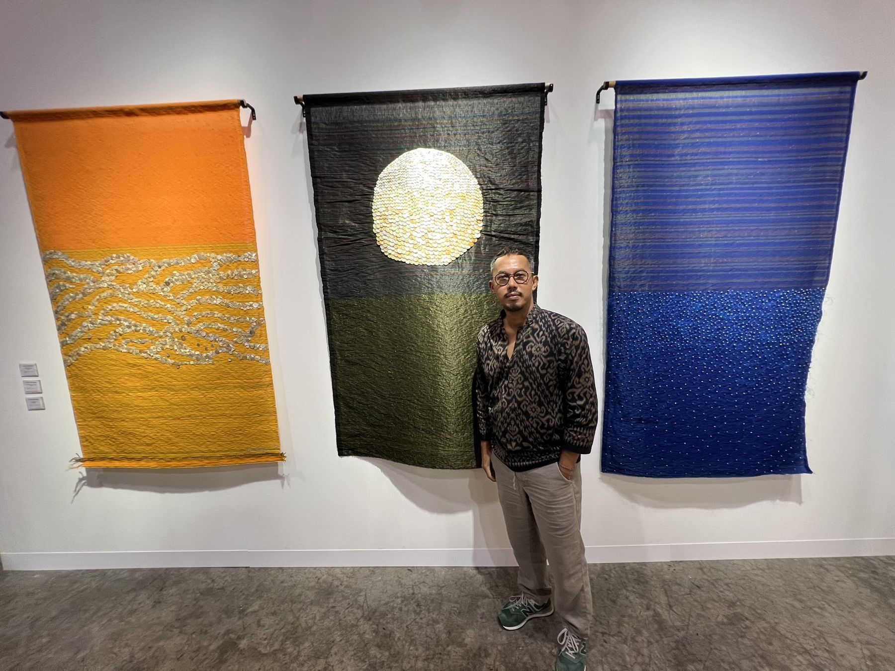 Iain Dawson standing between large woven textile works at an art fair