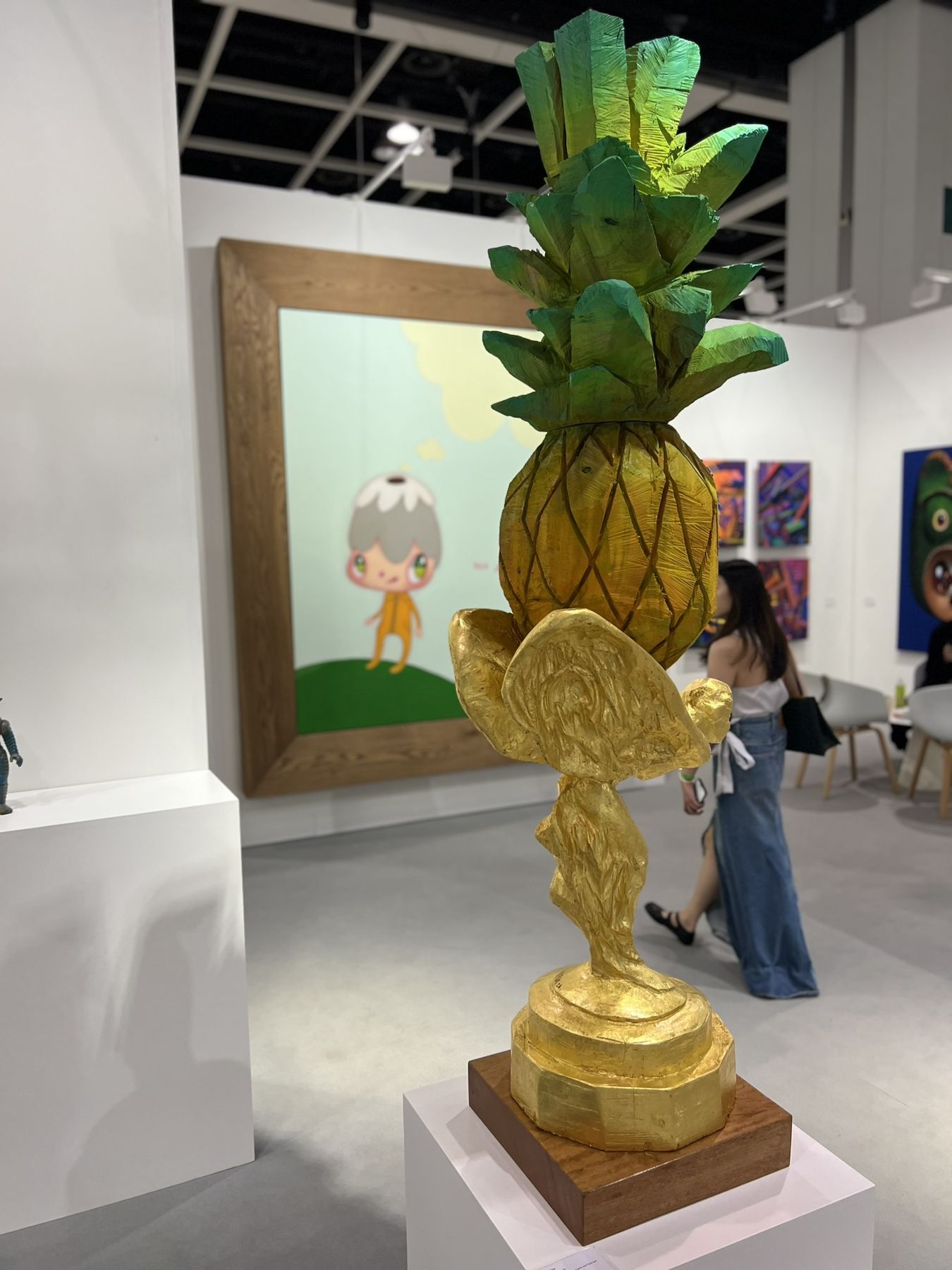 A gilded pineapple sculpture on a plinth in front of a large painting